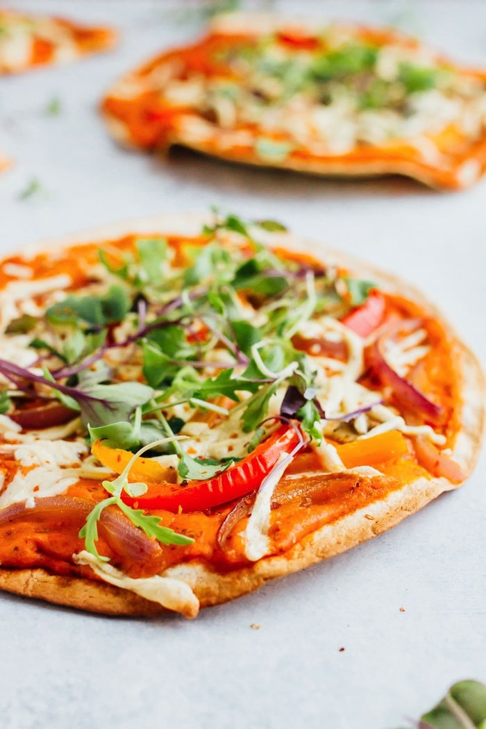 Tortilla pizzas topped with vegan cheese, peppers and greens and hummus.