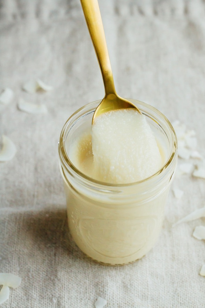 Coconut butter in a small mason jar with a spoonful on a gold spoon. 