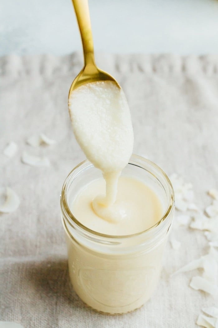 Coconut butter in a small mason jar with a spoonful on a gold spoon. 