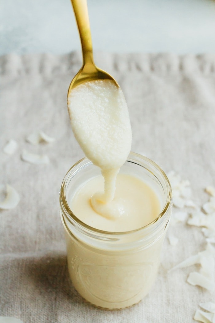 Coconut butter in a small mason jar with a spoonful on a gold spoon. 