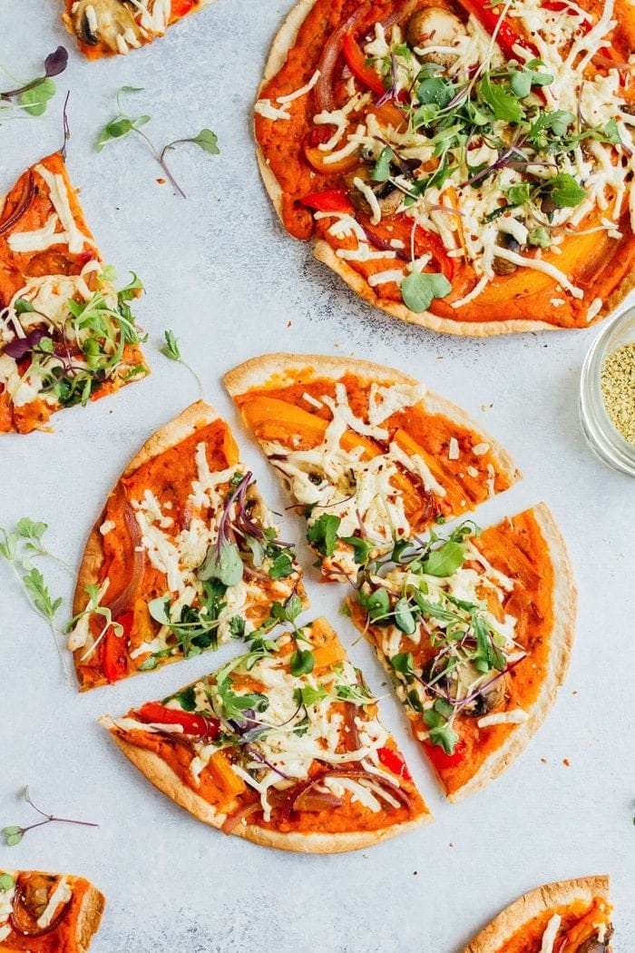 Tortilla pizzas topped with vegan cheese, peppers and greens and hummus.