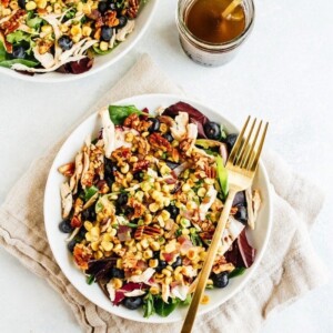 Two plates with blueberry corn chicken salad with a fork, cloth napkin and dressing on the side.