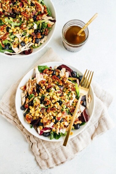 Two plates with blueberry corn chicken salad with a fork, cloth napkin and dressing on the side.