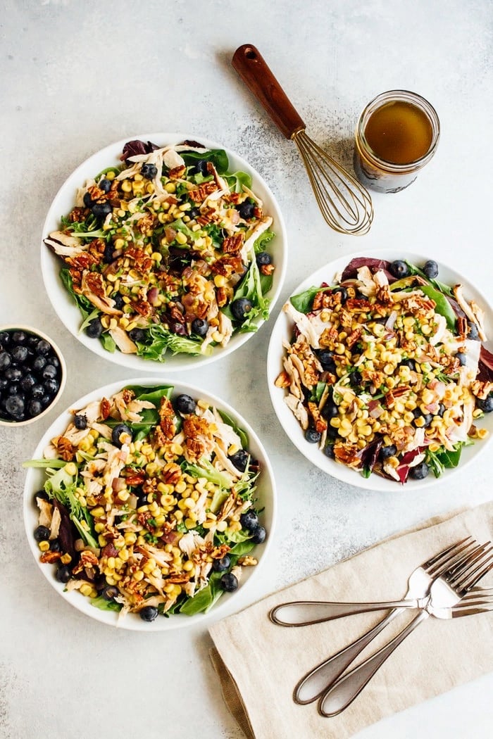Blueberry corn chicken salad in three bowls, with forks, napkins and a whisk.