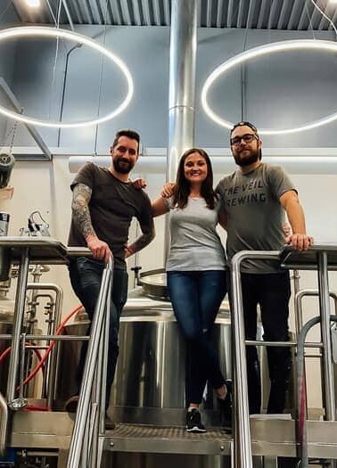 Three people standing in The Veil Brewing Co.