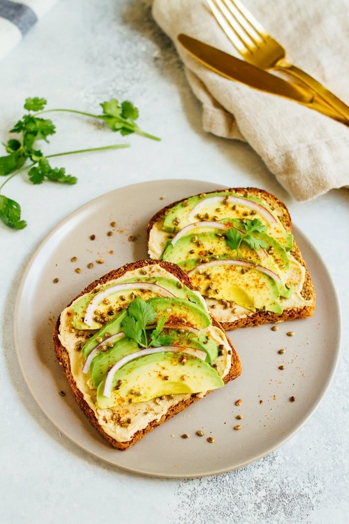 Hummus avocado toast makes for a quick and easy breakfast or snack idea. Load up each slice with red onion, cilantro and toasted hemp seeds for extra flavor and crunch. 
