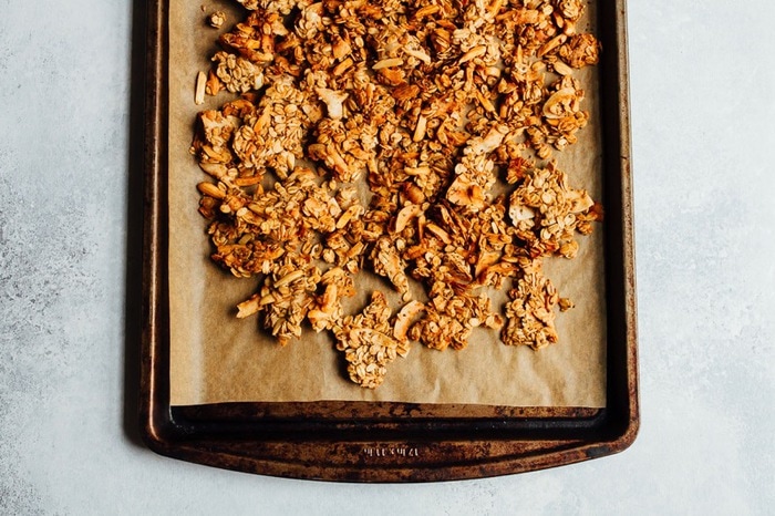 Granola on parchment and a baking sheet.