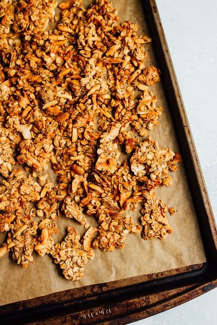 Baking sheet with parchment on diagonal, full of granola.