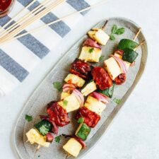 Grilled BBQ tempeh and veggie skewers on an oval platter, next to skewers on a towel.