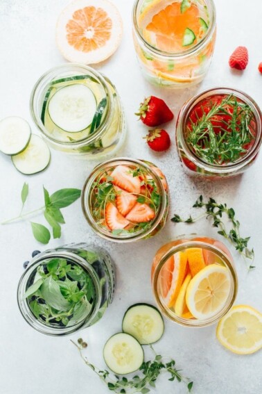 Top down view of fruit and herb infused waters, surrounded by slices of lemon, cucumber, strawberries and grapefruit on the table.