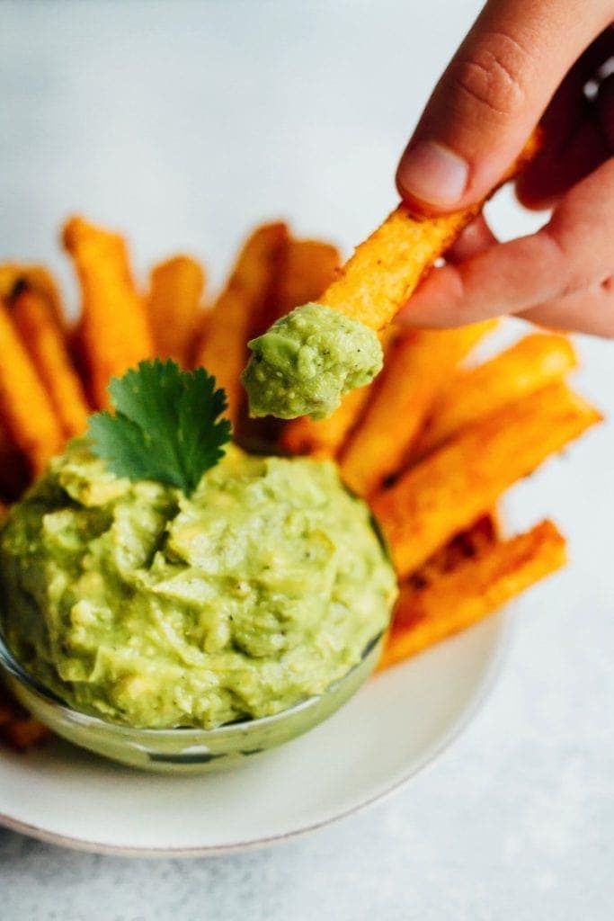 Hand holding a jicama fry and dipping it into a glass bowl of guacamole.