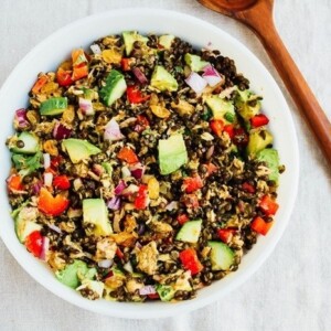 Lentil tuna salad in a bowl with vegetables and a wooden spoon.