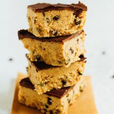 Stack of four no bake cookie dough bars topped with chocolate.