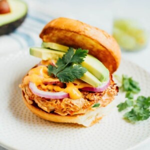 Open salmon burger with avocado cilantro, sriracha mayo, and purple onion.