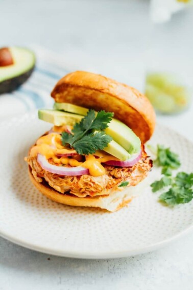 Open salmon burger with avocado cilantro, sriracha mayo, and purple onion.