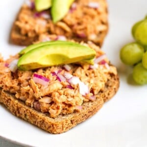 Tuna hummus bbq sandwich topped with avocado and grapes on the side.