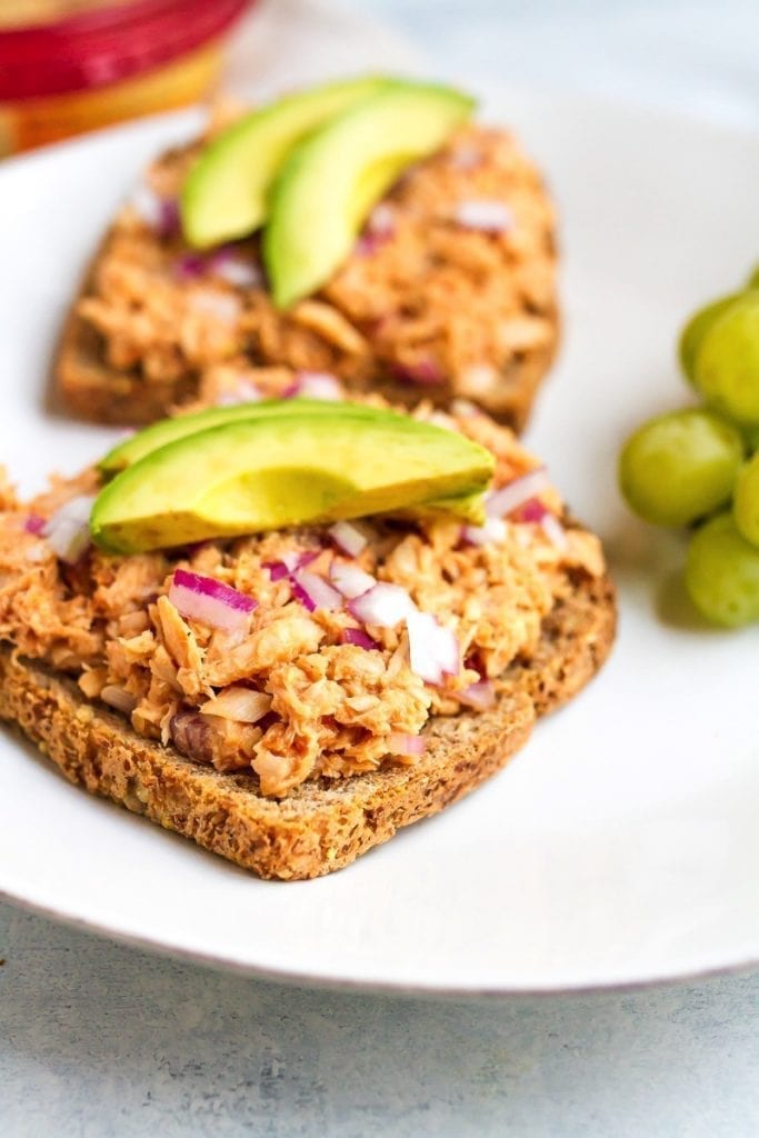 Tuna hummus bbq sandwich topped with avocado and grapes on the side.