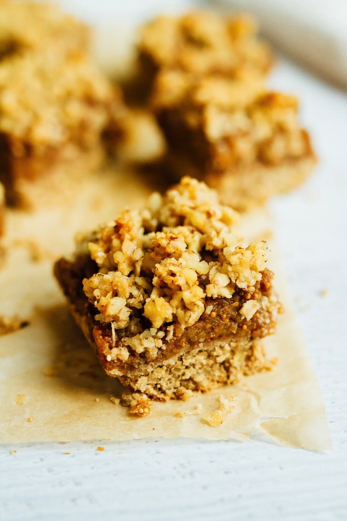 Wholesome Fig Jam Crumble Bars you can feel good about enjoying for breakfast, a snack or dessert. They’re loaded with healthy fats and naturally sweetened. Close up of a fig crumble bar on parchment.
