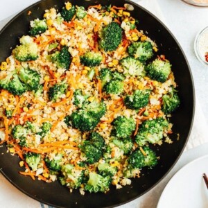 Cauliflower rice with carrots, corn, and broccoli in a pan.=