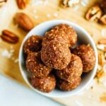 Pecan energy bites in a white bowl on a wooden cutting board.