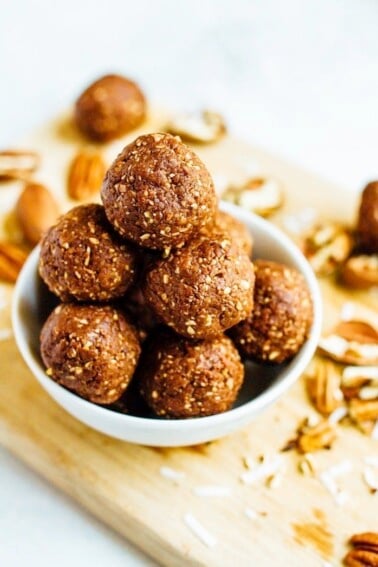 Pile of pecan energy bites in a bowl on a wooden cutting board with pecans.