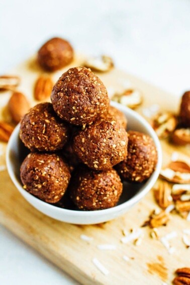 Pile of pecan energy bites in a bowl on a wooden cutting board with pecans.