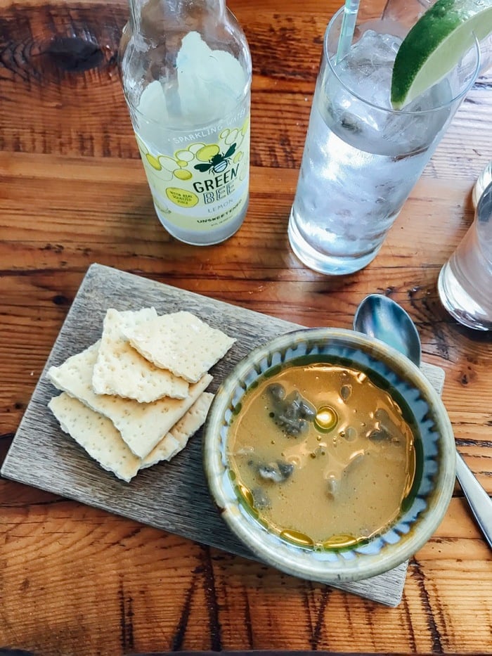Coconut green curry broth with maitake mushrooms and crackers on a wood slate with sparkling Green Bee water.