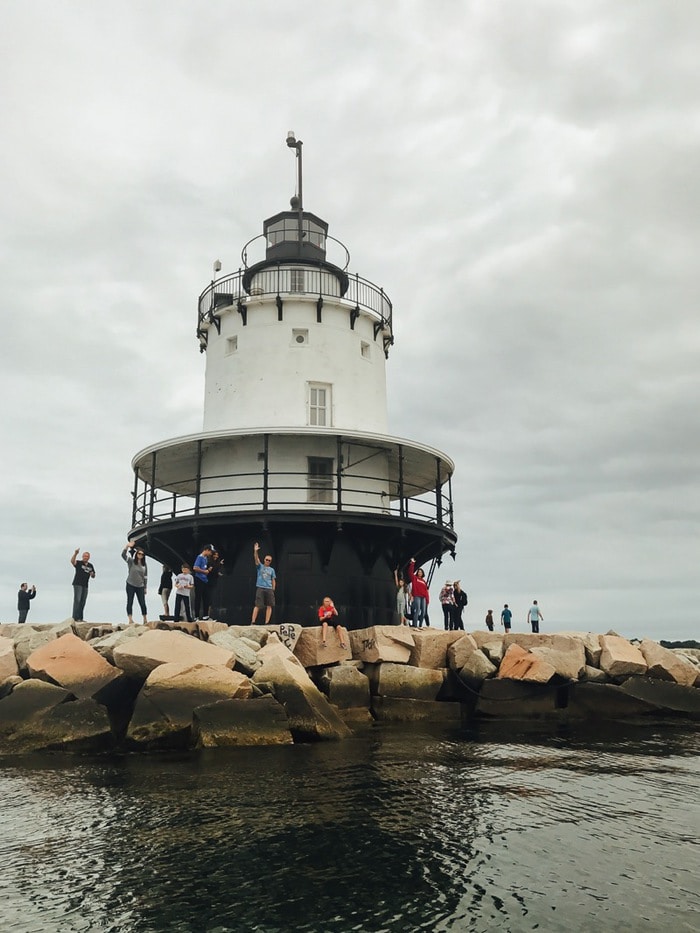 Lighthouse with people waving below, next to the Portland Maine coast.