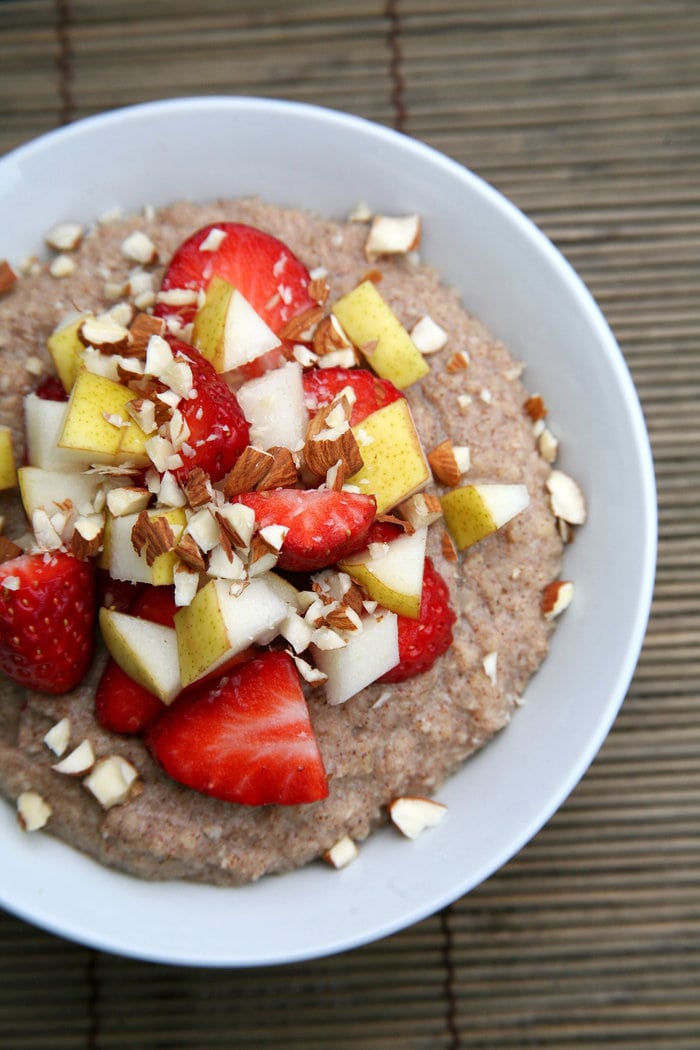 A bowl of cauliflower porridge with strawberry, apple, and almond topping.