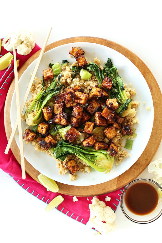 Overhead shot of crispy peanut tofu cauliflower rice stir fry on a white plate with chopsticks.