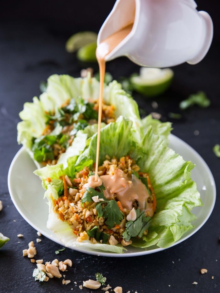 Cauliflower rice lettuce cups with sriracha peanut sauce in white serving dish.