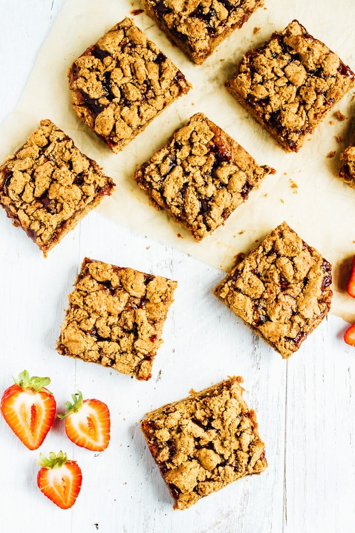 Peanut Butter and Jelly Crumble Bars // Gluten-free PB&J crumble bars lying on a table and parchment paper. Sliced strawberries are to the side.