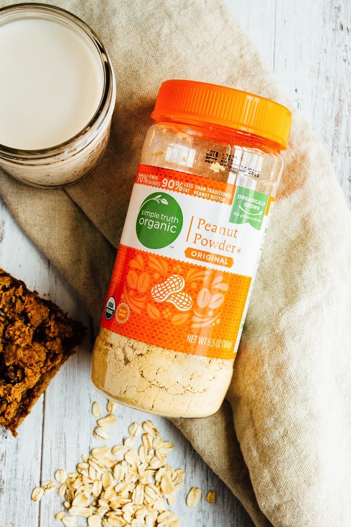 Jar of Simple Truth Organic Peanut Butter Powder laying on a kitchen towel and next to a glass of almond milk.