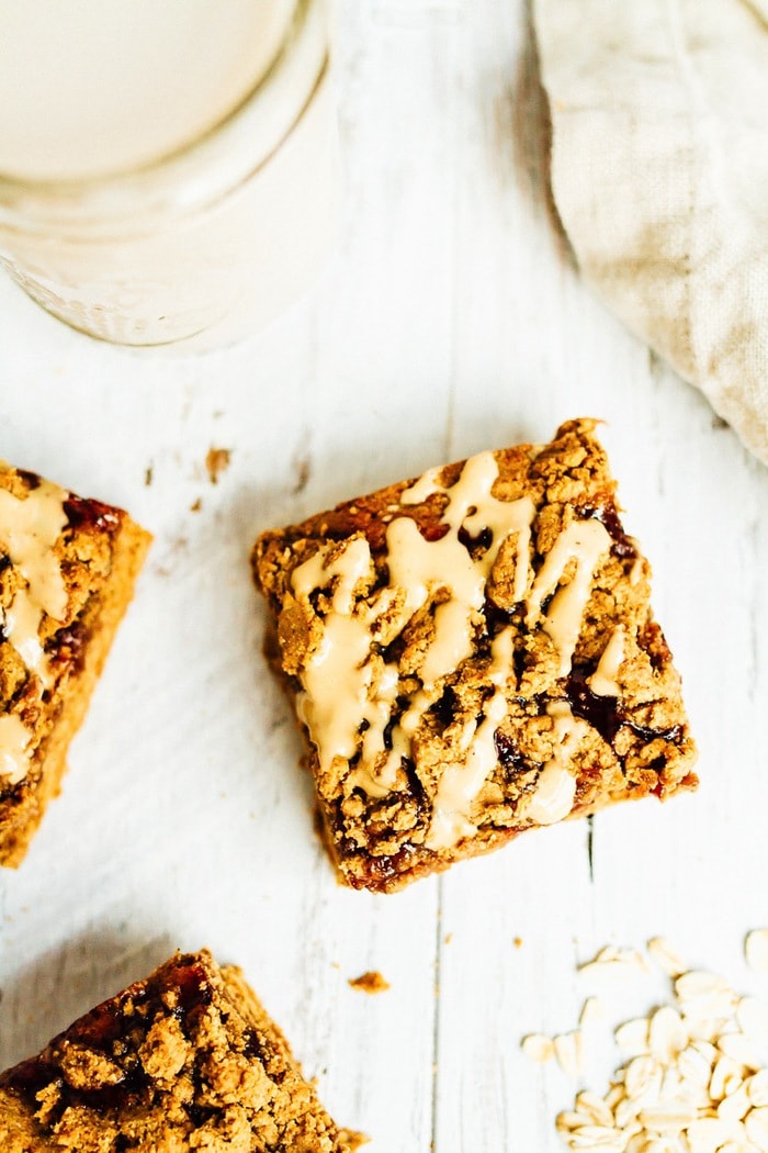 Peanut Butter and Jelly Crumble Bars // Gluten-free PB&J crumble bar drizzled with peanut butter. Glass of milk to the size.