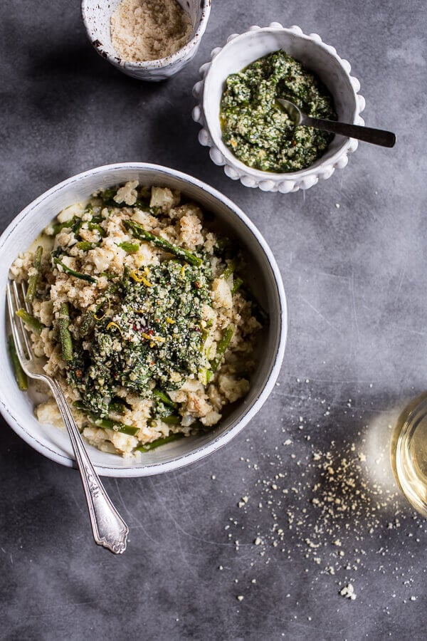 Cauliflower risotto with asparagus cilantro basil hemp seed pesto in a white bowl with additional pesto nearby.