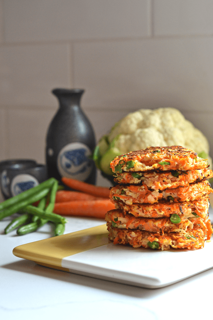 A stack of cauliflower fried rice fritters on a two-tone serving platter.