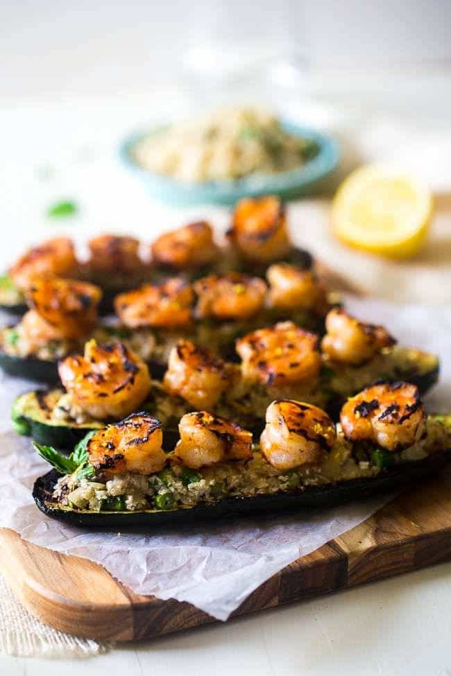 4 cauliflower stuffed grilled zucchini with shrimp on a wooden serving platter.