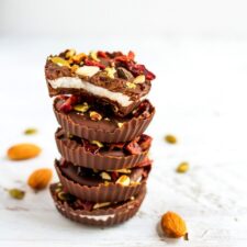 Stack of dark chocolate coconut butter cups, topped with seeds and nuts.