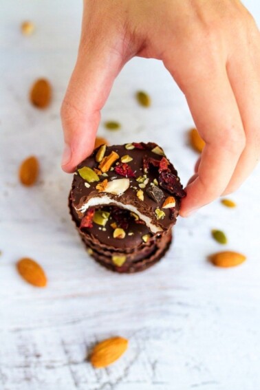 Hand grabbing a coconut butter cup with a bite taken out of it, off of a stack of coconut butter cups.