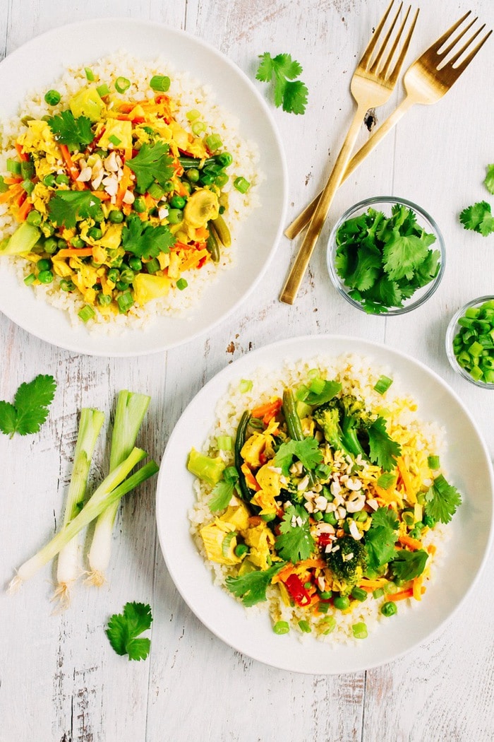 Two bowls of tuna curry with cauliflower rice, filled with green veggies and topped with cilantro and chopped peanuts. Bowls on a table next to green onions, two forks, and cilantro.