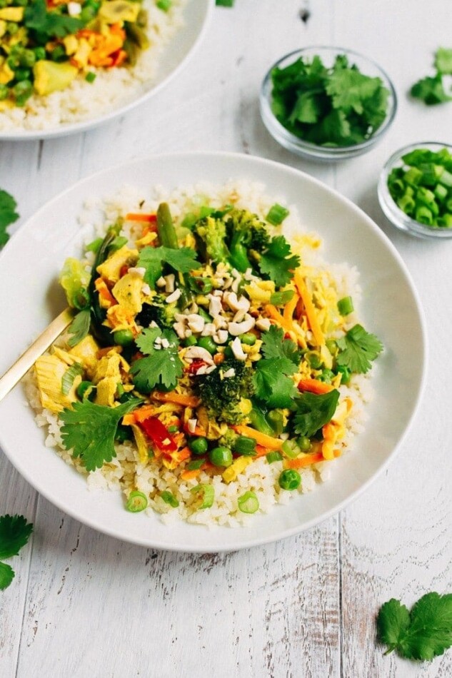 Tuna curry with vegetables over cauliflower rice in a white bowl, with small bowls of cilantro and green onion on the side.