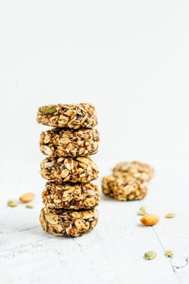 Stack of five granola bites on white wood with a few more in the background.