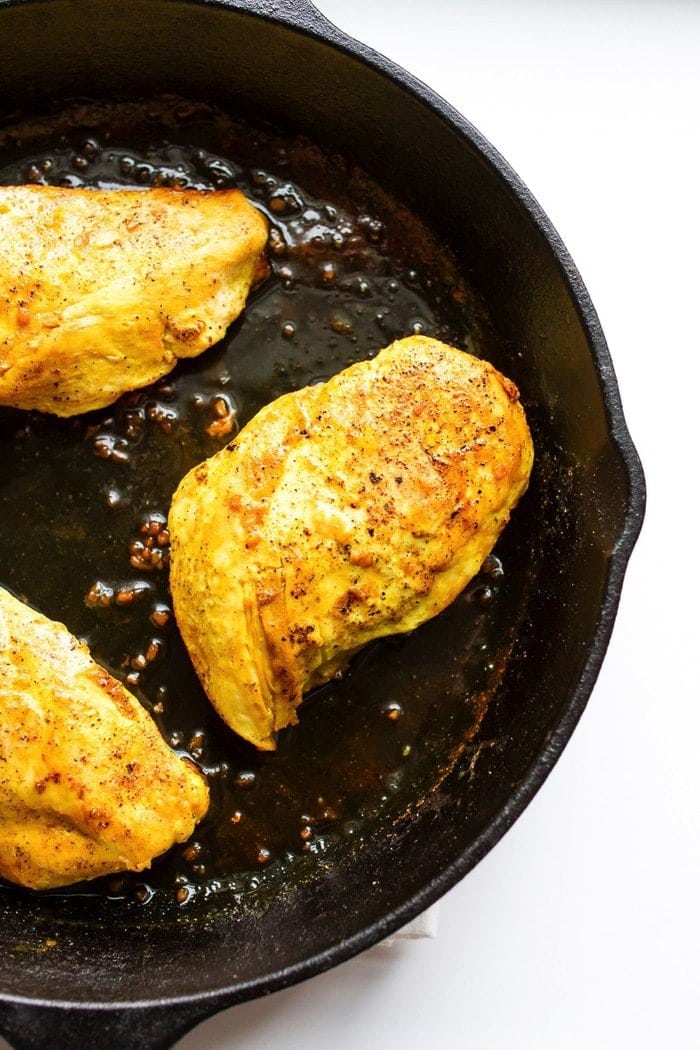 Chicken fully seasoned with maple syrup and ground turmeric in the cast iron skillet.