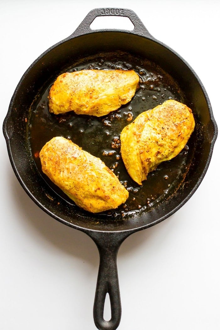 Overhead shot of maple turmeric chicken in cast-iron skillet, white background.