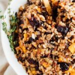 Bowl of wild rice stuffing with butternut squash and sweet cherries topped with thyme.