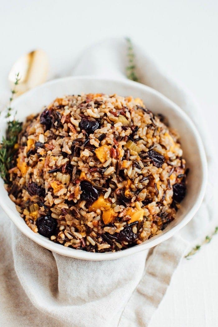 Bowl of wild rice stuffing with butternut squash and sweet cherries topped with thyme.