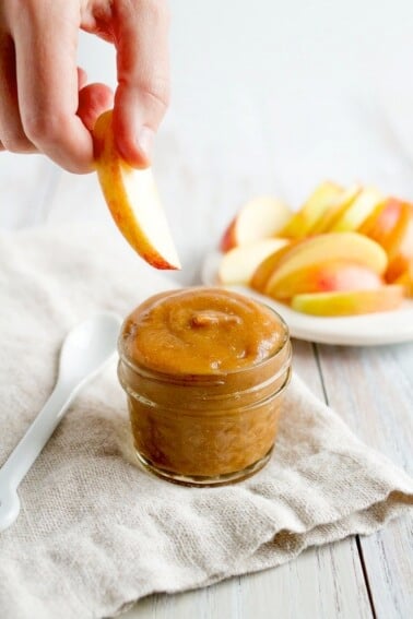 A hand dipping an apple into date caramel in a small jar.