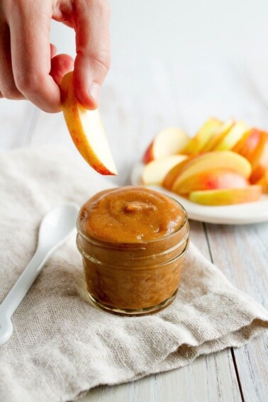 A hand dipping an apple into date caramel in a small jar.