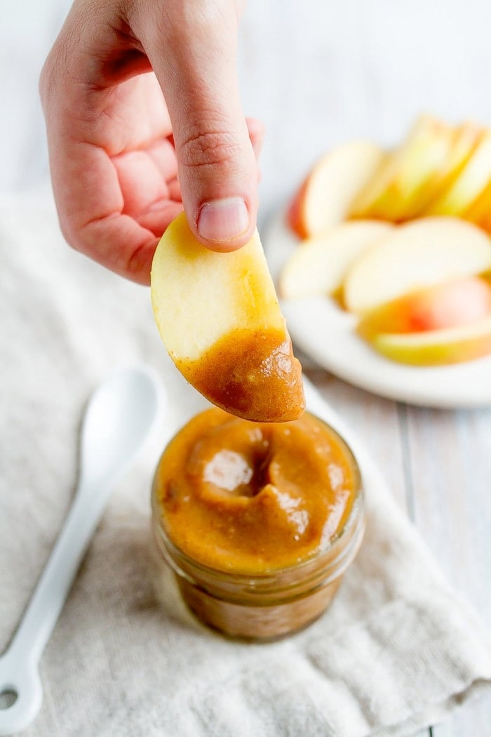 A hand holding up a slice of apple that was dipped into the date caramel sauce.