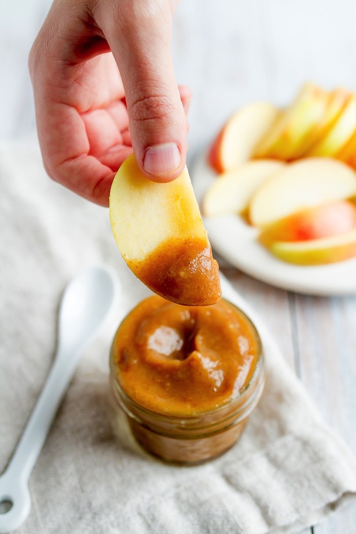 A hand holding up a slice of apple that was dipped into the date caramel sauce.